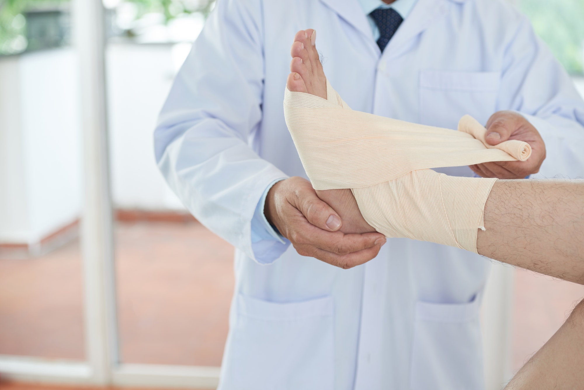 Unrecognizable doctor bandaging foot of patient
